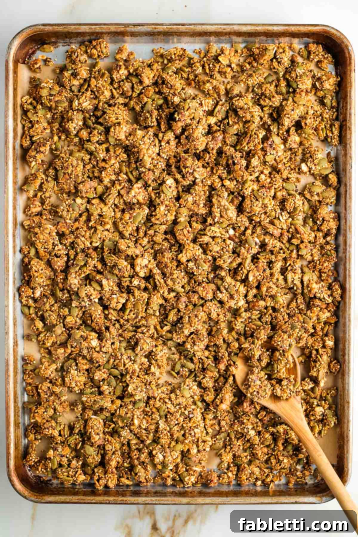 Cozy Pumpkin Spice Granola 14 Wooden spoon, pushing around clusters of granola on a large rimmed baking sheet.