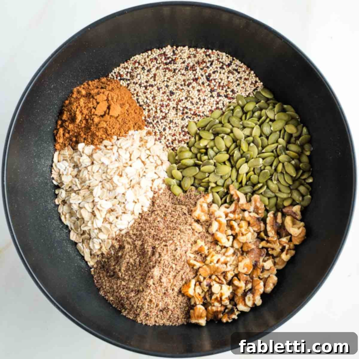 Cozy Pumpkin Spice Granola 5 Sections in a bowl of pumpkin seeds, oats, walnuts, ground flax, dry quinoa, pumpkin pie spice.