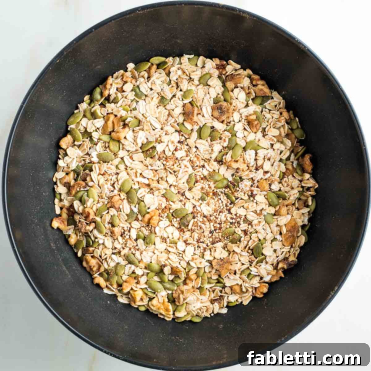 Cozy Pumpkin Spice Granola 6 Mixture of nuts, seeds, ground flax, spices and dry quinoa in a black bowl.