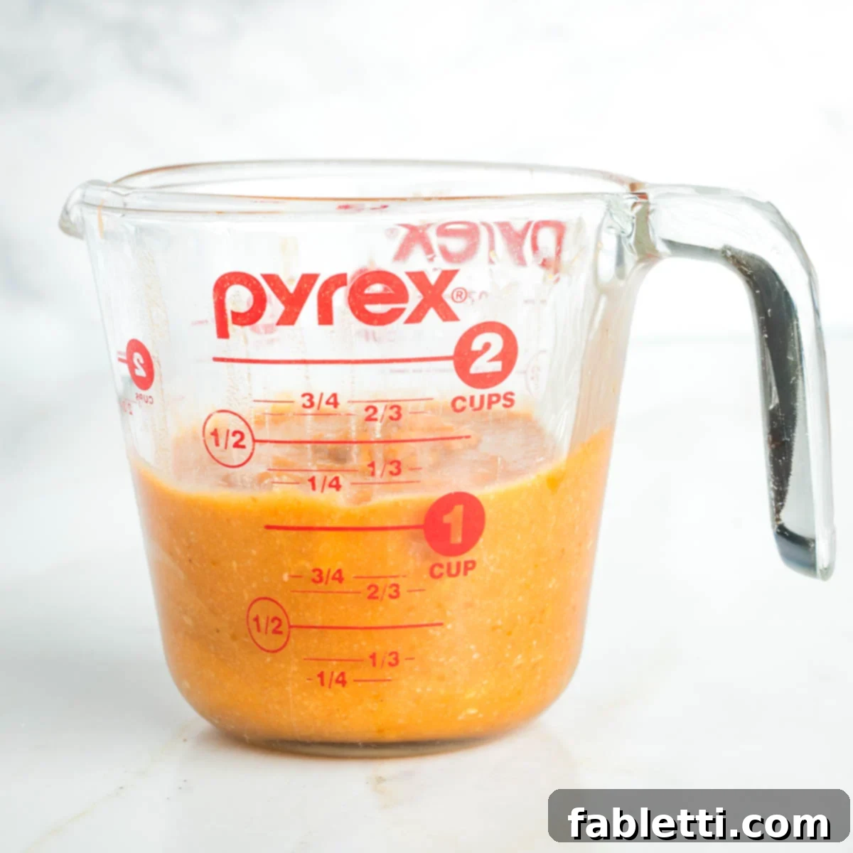 Cozy Pumpkin Spice Granola 8 Orange pumpkin mixture in a glass measuring cup.