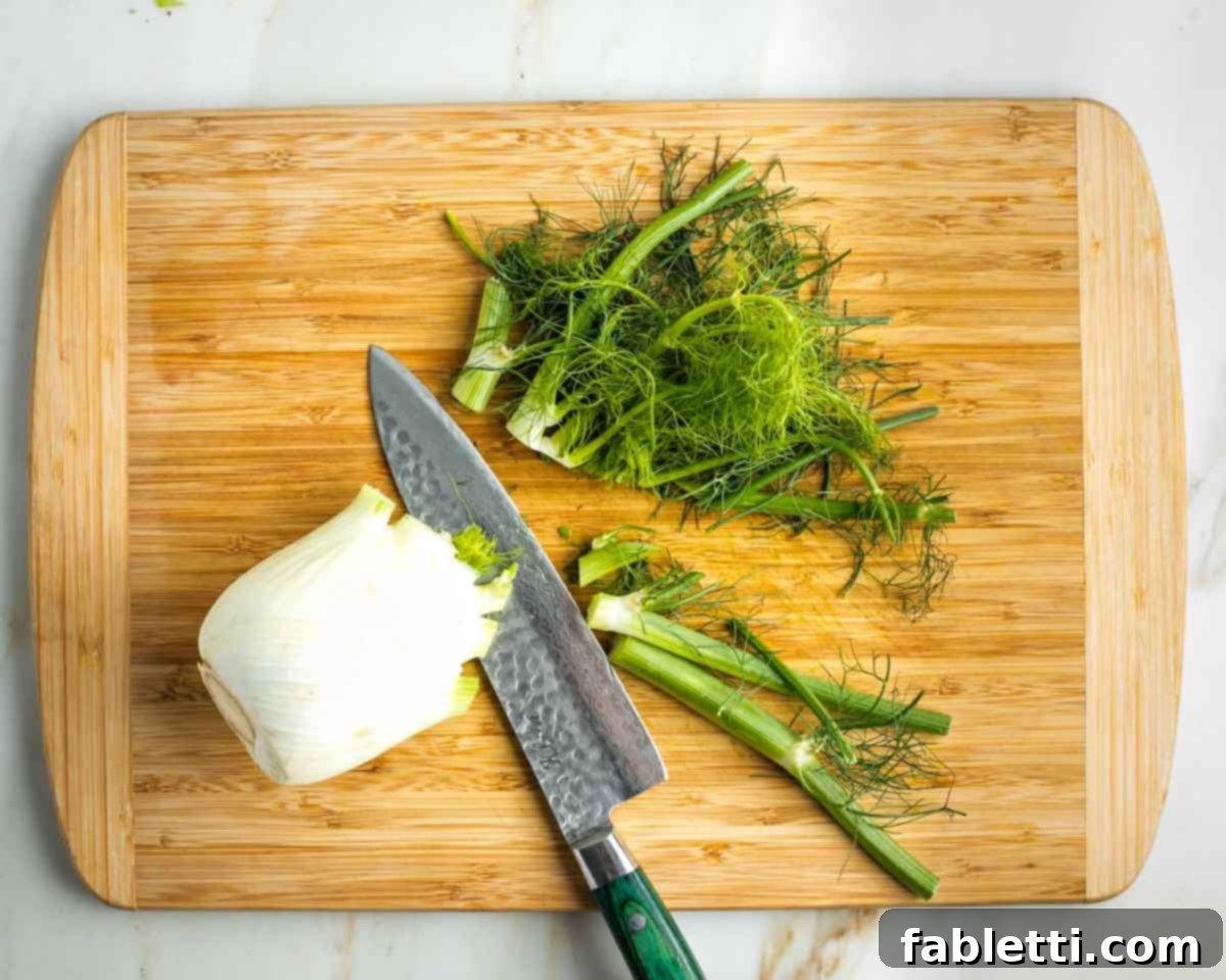 Vibrant Apple Fennel Farro Salad with Pomegranate Gems 11 A close-up view of a chef carefully cutting off the top fronds from a fresh bulb of fennel, a preparatory step before slicing the bulb.