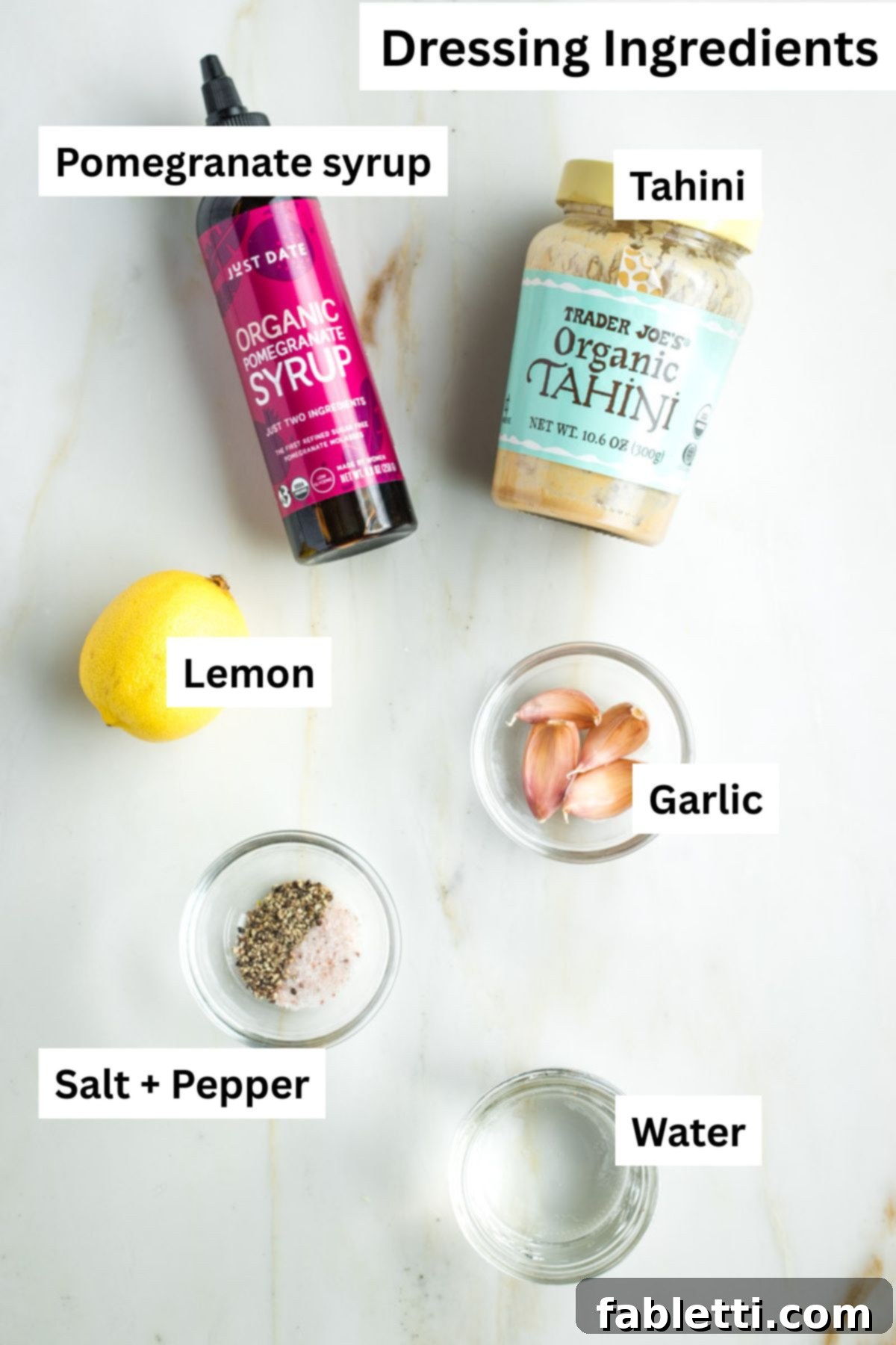 Vibrant Apple Fennel Farro Salad with Pomegranate Gems 4 Labeled ingredients for the pomegranate tahini dressing: dark pomegranate syrup, creamy tahini, a fresh lemon, garlic cloves, water, salt, and black pepper.