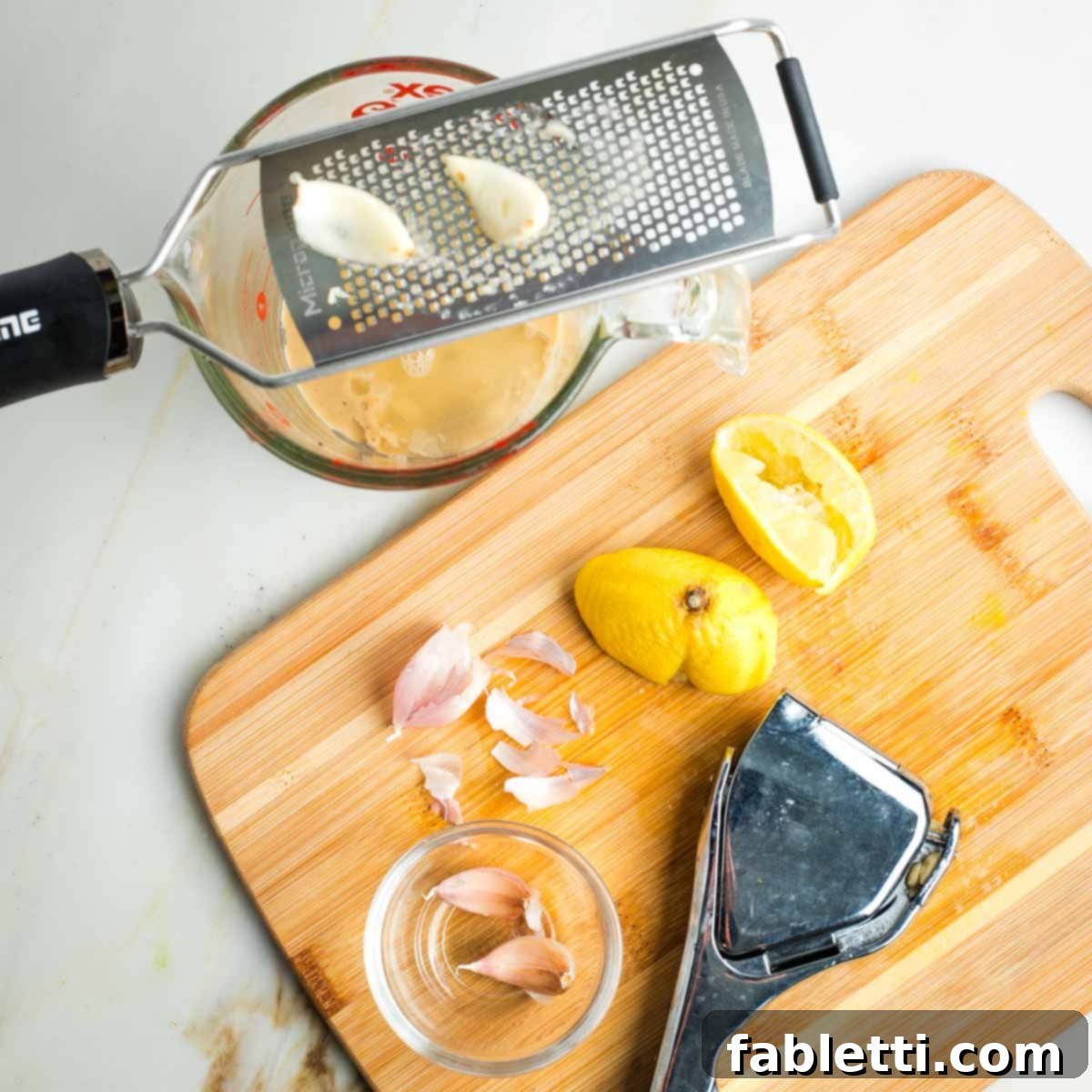 Vibrant Apple Fennel Farro Salad with Pomegranate Gems 5 A microplane grater is used to zest fresh garlic directly over a glass measuring cup containing tahini and freshly squeezed lemon juice, preparing the base of the dressing.