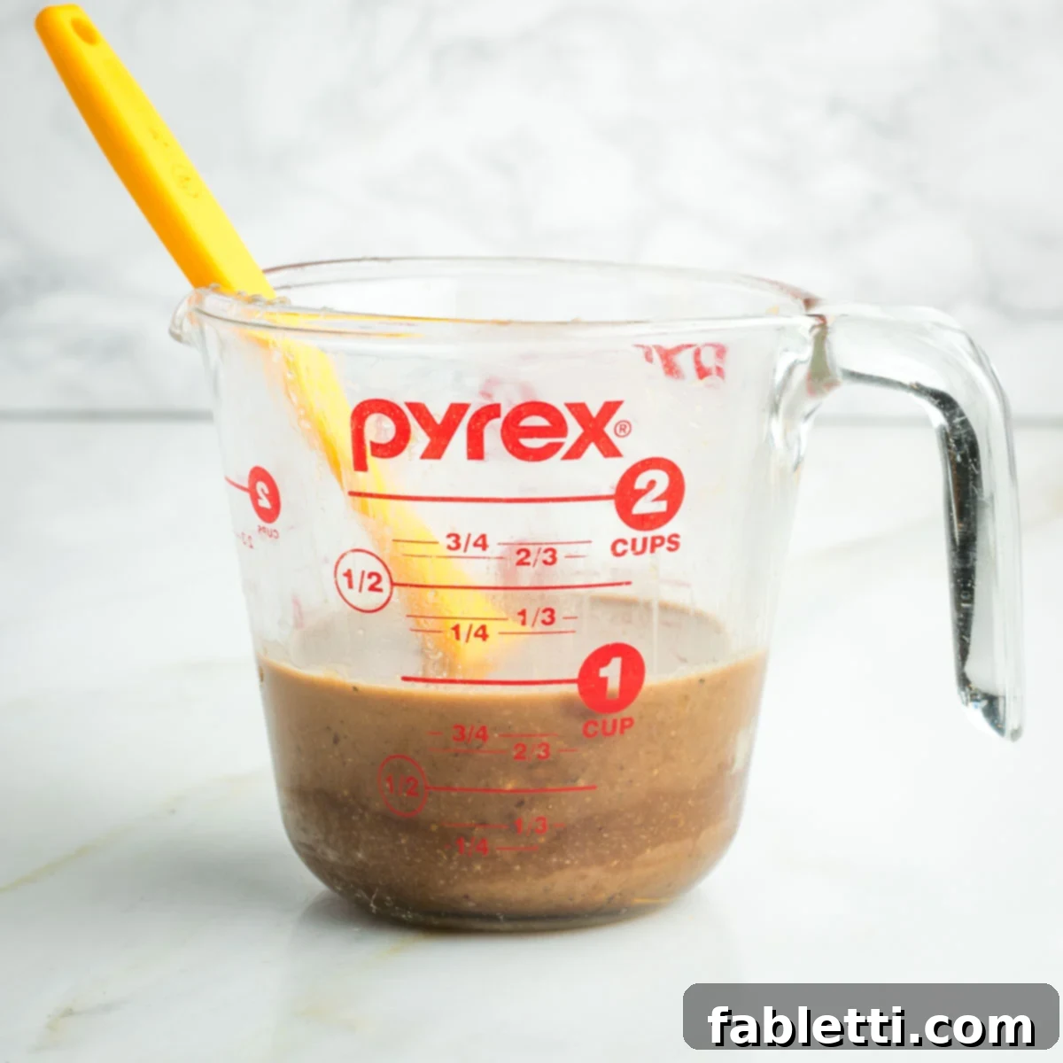 Vibrant Apple Fennel Farro Salad with Pomegranate Gems 6 A small whisk is stirring together the tahini and pomegranate syrup dressing in a glass measuring cup, creating a smooth and emulsified consistency for the apple and fennel salad.