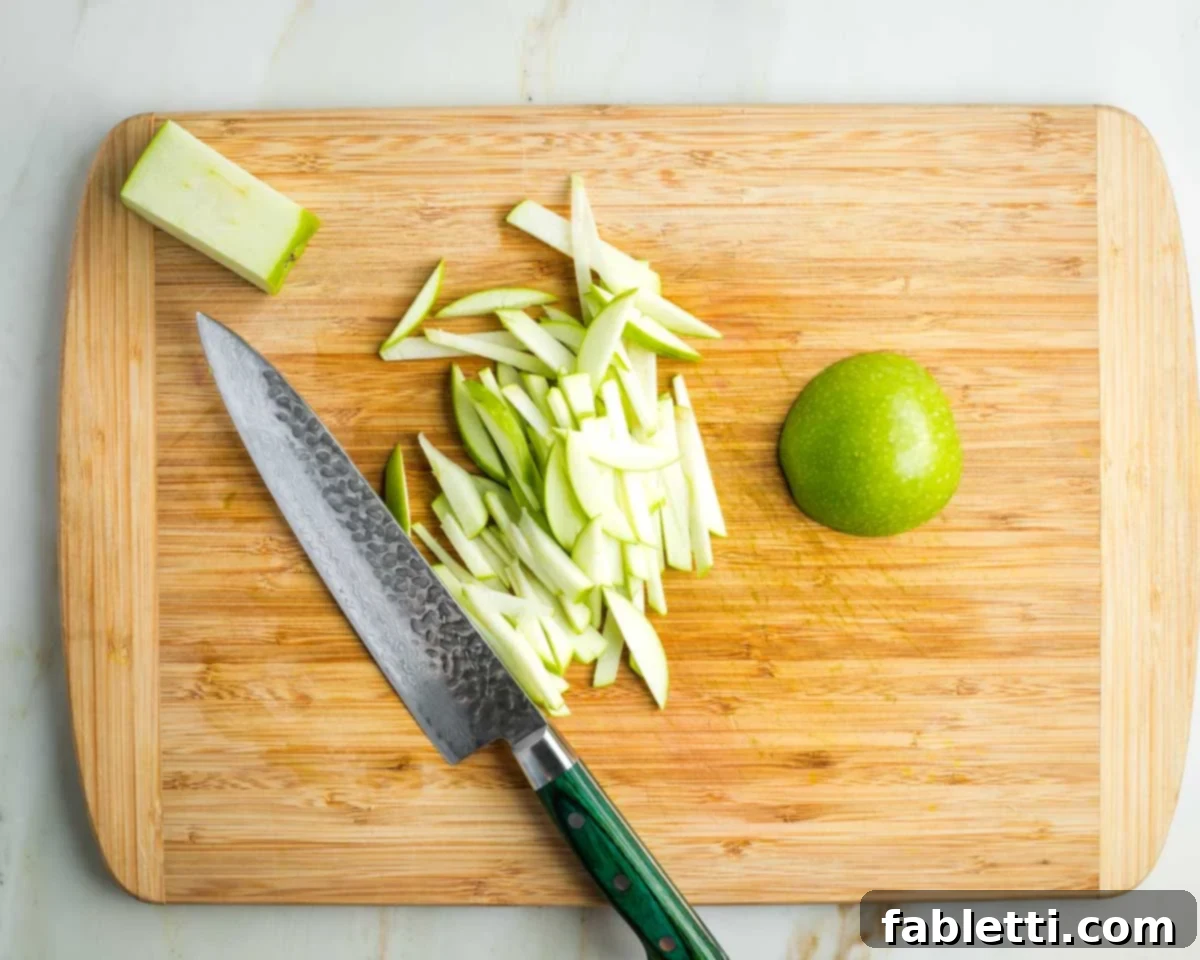 Vibrant Apple Fennel Farro Salad with Pomegranate Gems 10 A green apple is being skillfully cut into thin, uniform strips on a cutting board, demonstrating the precision needed for salad preparation.