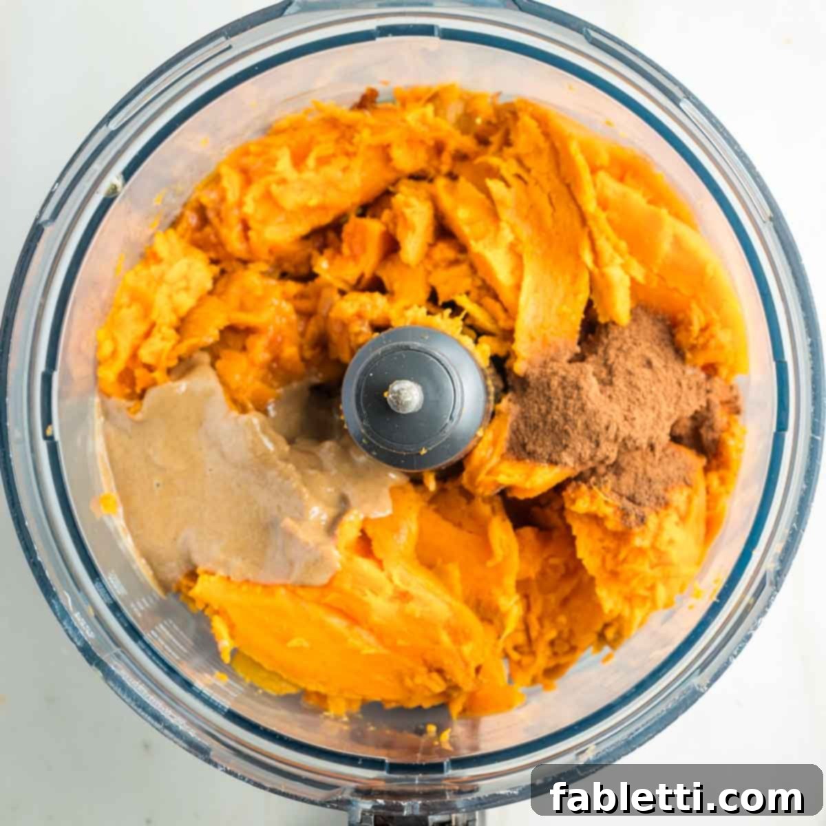 Golden Maple Pecan Sweet Potato Casserole 13 Bowl of a food processor with baked sweet potato pulp, tahini, maple syrup, cinnamon, allspice, and salt, before blending.