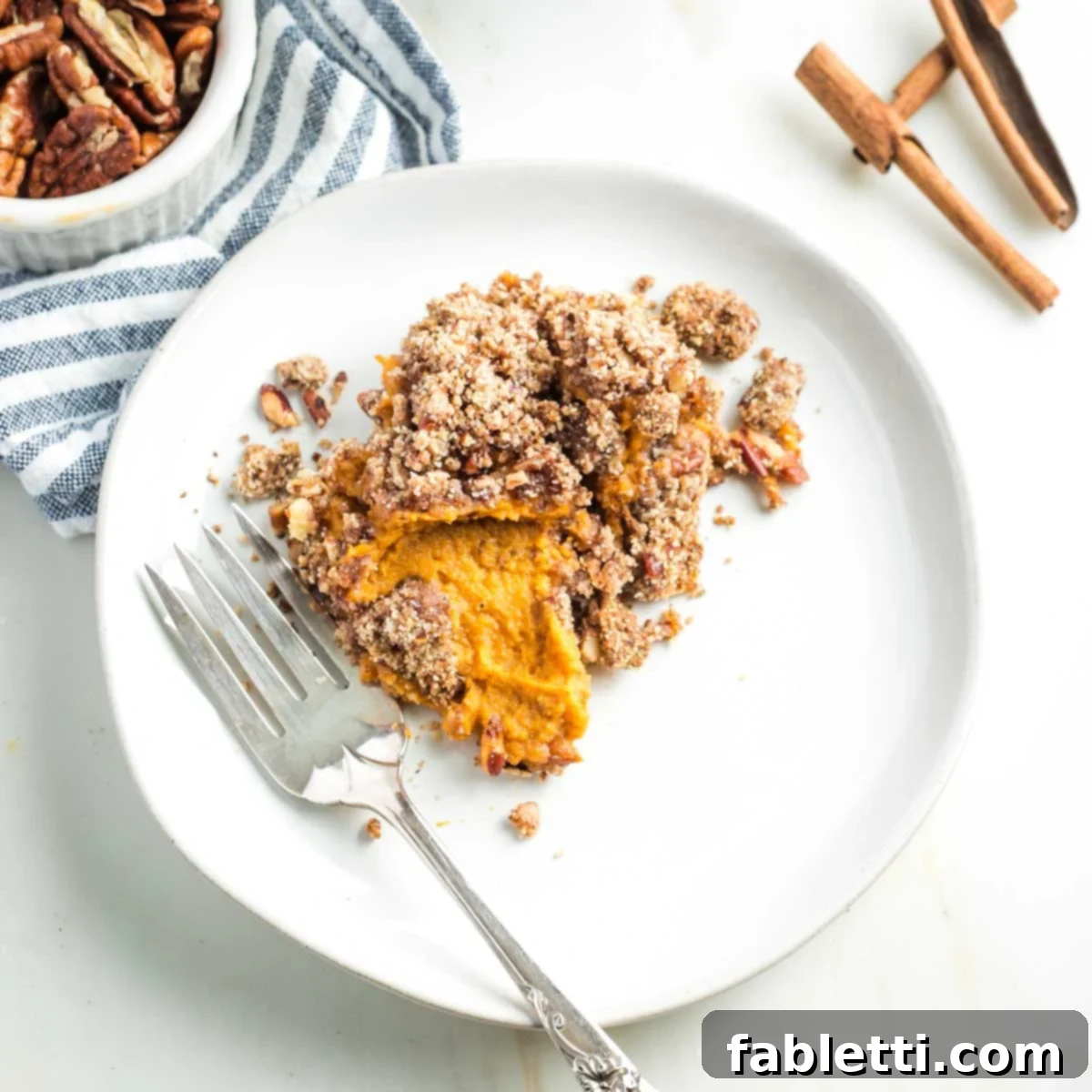 Golden Maple Pecan Sweet Potato Casserole 19 A plate and fork with a serving of sweet potato casserole, clearly showing the creamy orange potato mixture and the distinct, crunchy pecan crumble topping.