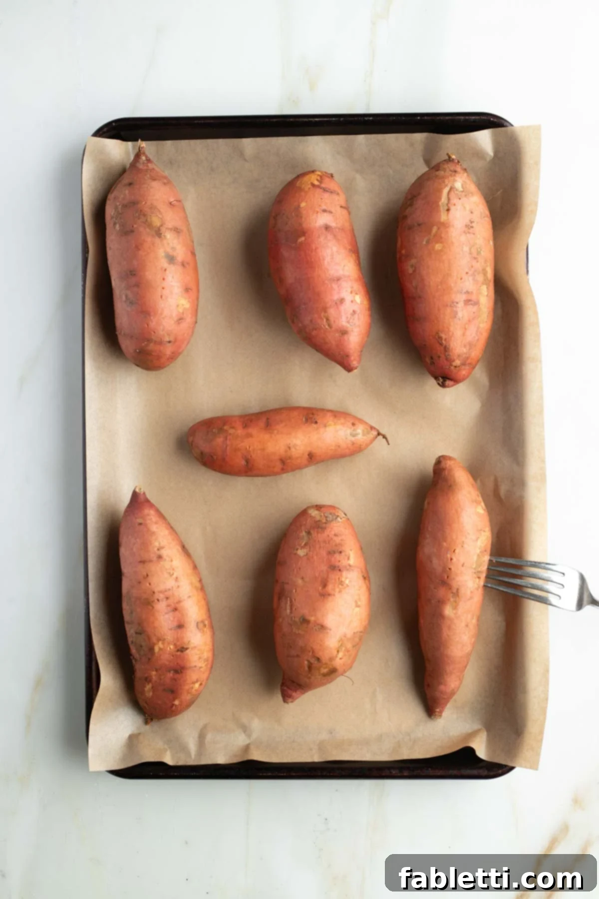 Golden Maple Pecan Sweet Potato Casserole 5 Sweet potatoes, lined up on a parchment-lined baking sheet, one being pierced with a fork before baking to allow steam to escape.