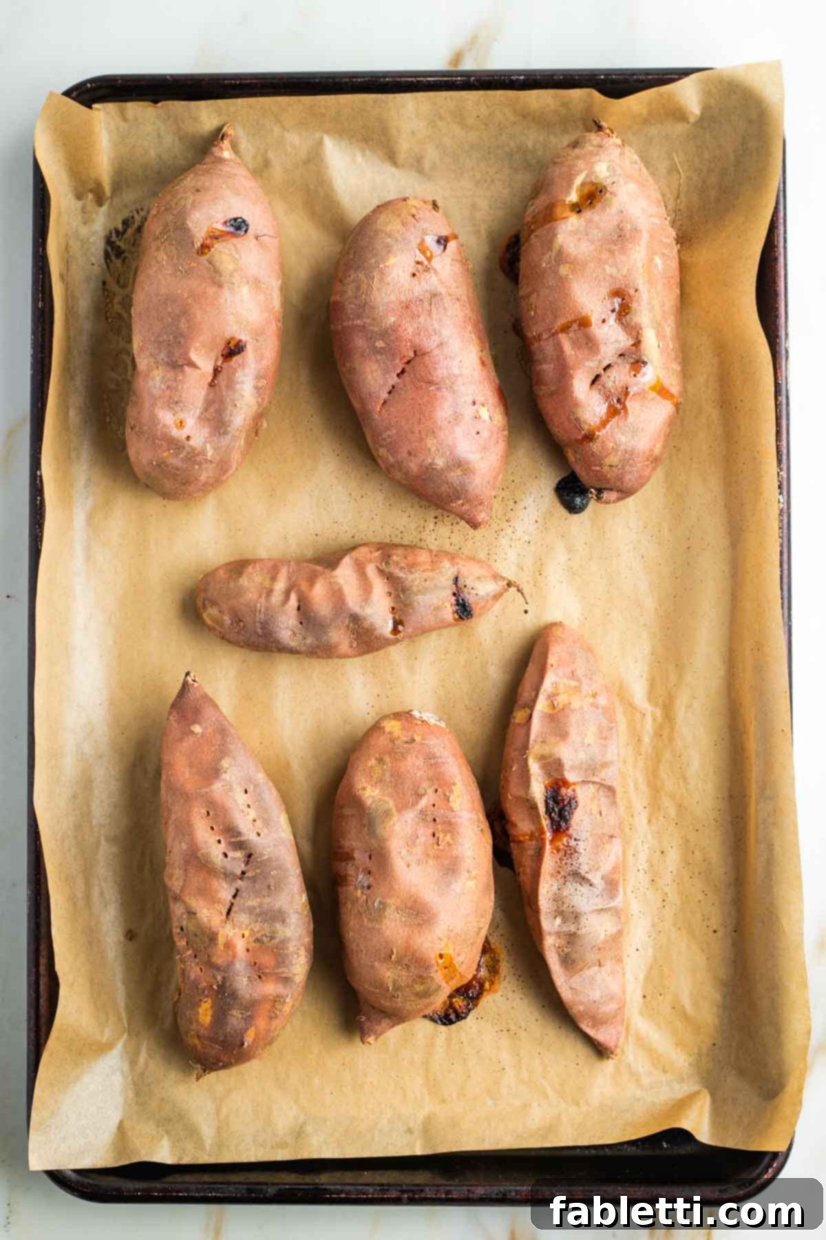 Golden Maple Pecan Sweet Potato Casserole 6 Shriveled baked sweet potatoes, still in their skins, on a baking tray after roasting to tender perfection.