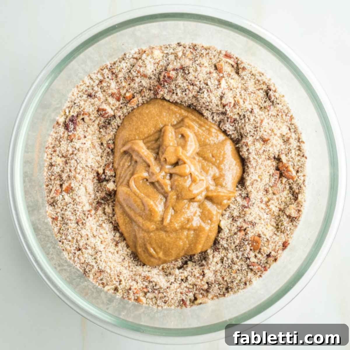 Golden Maple Pecan Sweet Potato Casserole 9 Tahini and maple syrup mixture being poured over the dry ingredients (pecans and flours) in a glass mixing bowl.