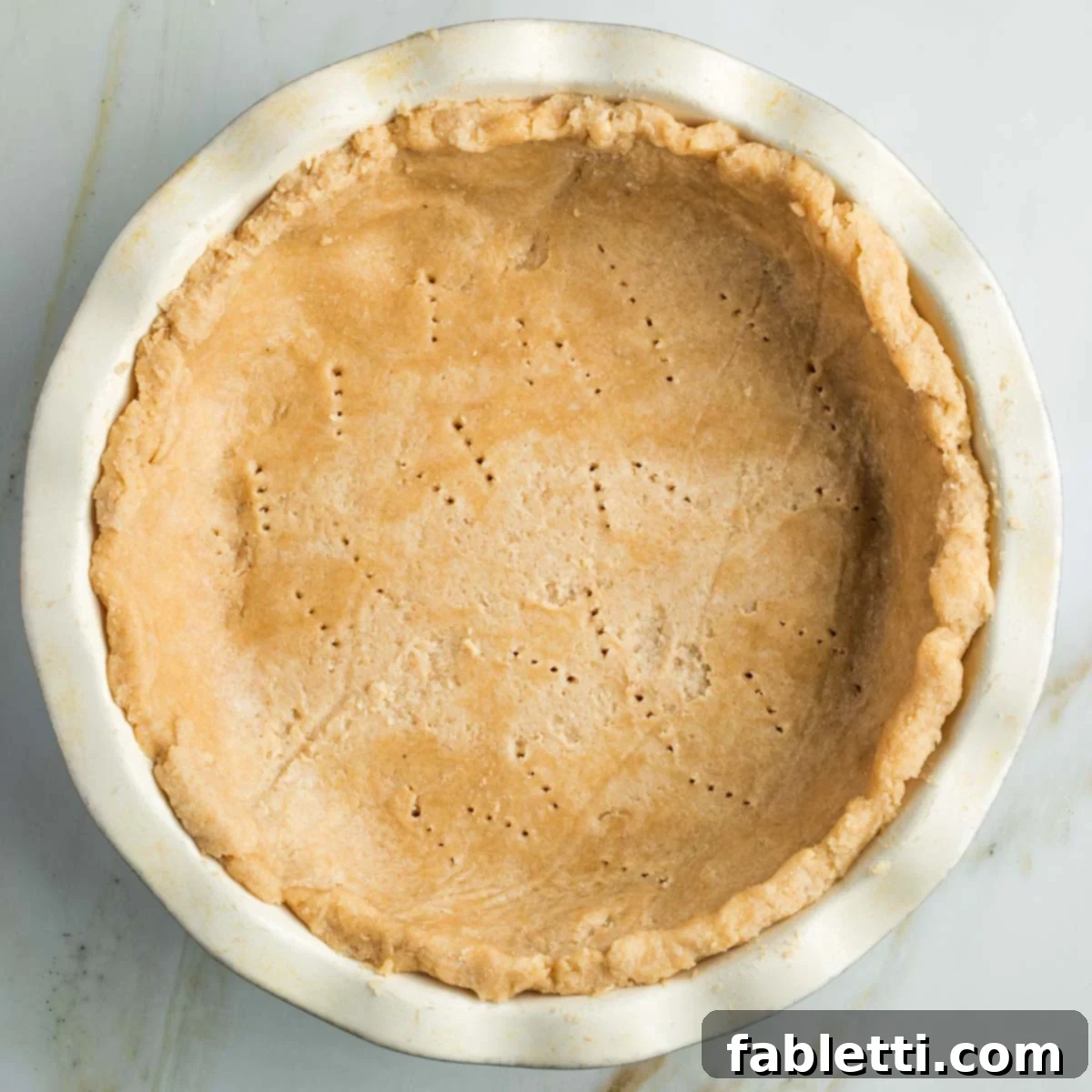 Effortless Vegan Pumpkin Pie with a Homemade Dairy-Free Crust 11 An unbaked vegan pie crust carefully pressed into a fluted ceramic pie plate, with fork tine marks visible on the bottom.