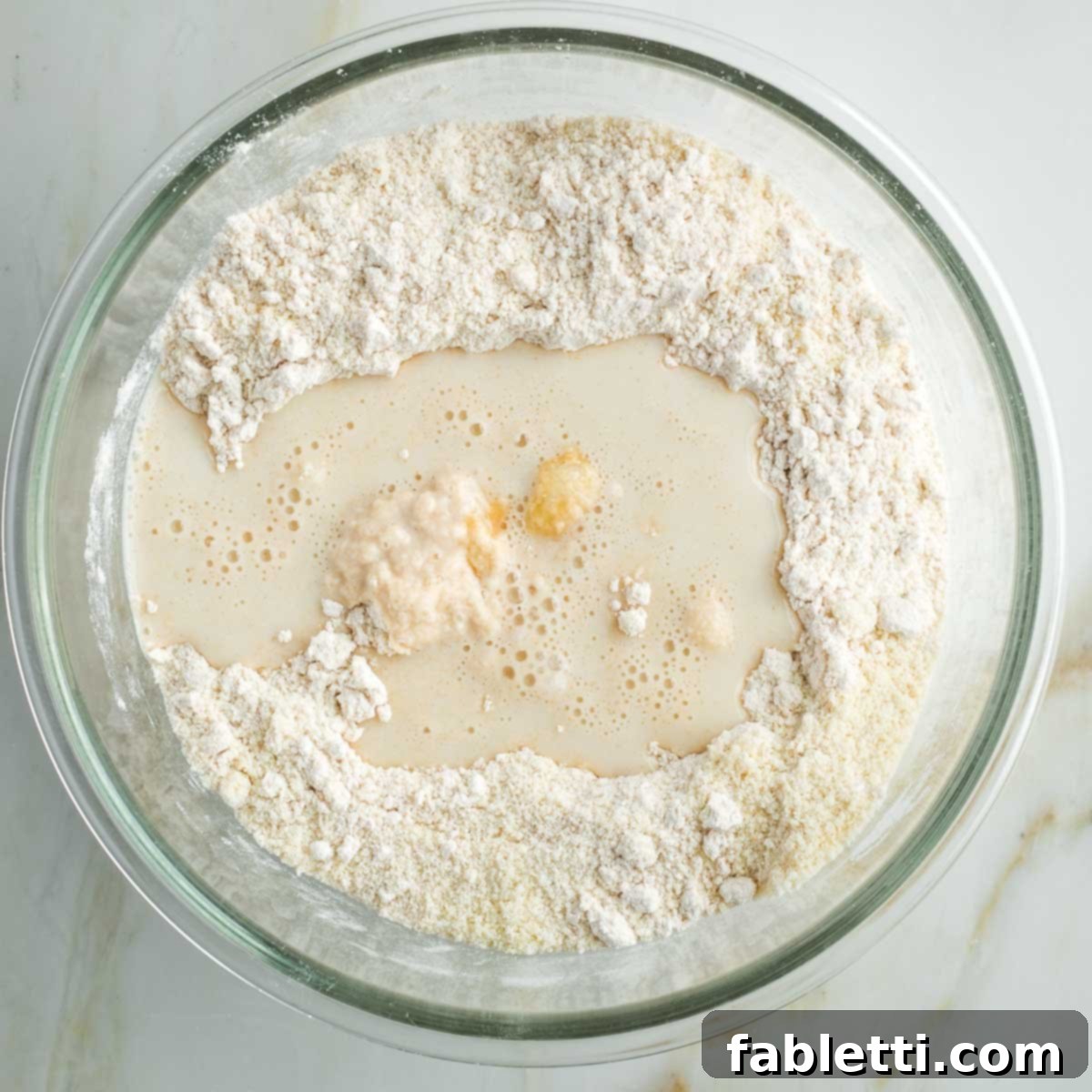 Effortless Vegan Pumpkin Pie with a Homemade Dairy-Free Crust 6 Liquid ingredients, almond milk and maple syrup, being poured into the dry flour mixture in a glass bowl for the vegan pie crust.