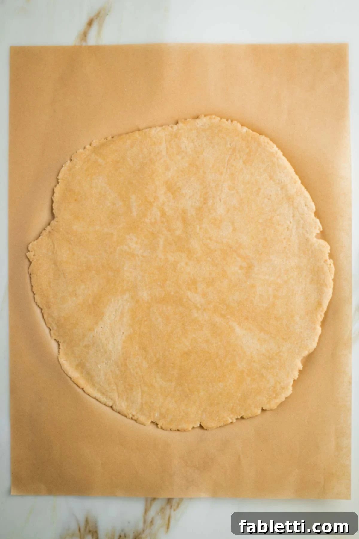 Effortless Vegan Pumpkin Pie with a Homemade Dairy-Free Crust 10 A roughly circular piece of thin vegan pie dough resting on unbleached parchment paper, ready to be transferred.