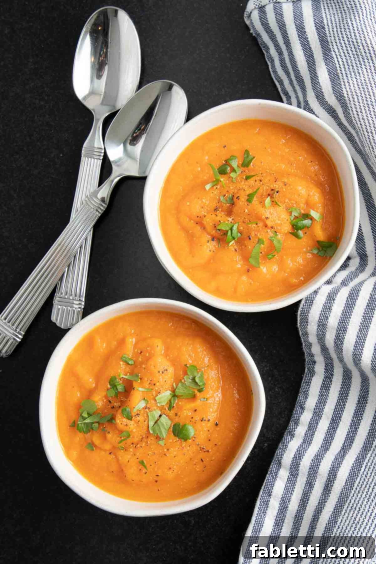 Golden Vegan Carrot Ginger Soup 2 Two bowls brimming with bright orange vegan carrot ginger soup, elegantly garnished with fresh parsley sprigs.