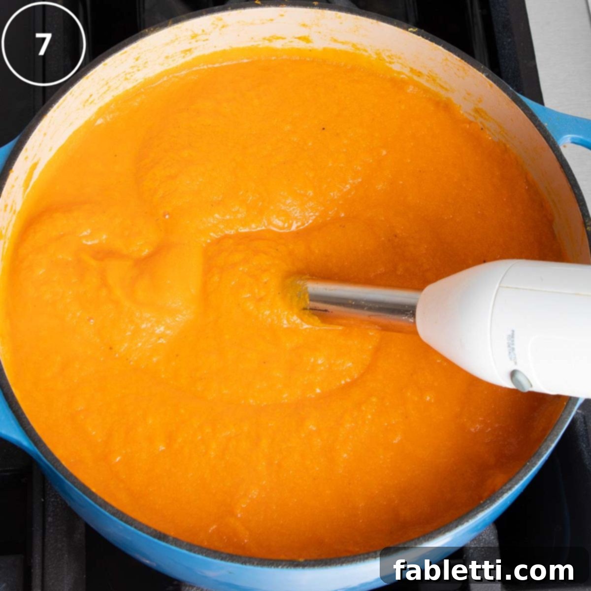 Golden Vegan Carrot Ginger Soup 14 A Dutch oven full of carrot ginger soup being pureed to a creamy consistency using an immersion blender.
