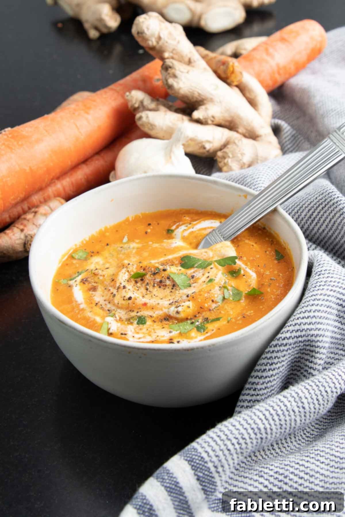 Golden Vegan Carrot Ginger Soup 17 A close-up of creamy carrot soup, elegantly swirled with vegan sour cream and generously sprinkled with fresh green herbs, showcasing its appealing texture and color.