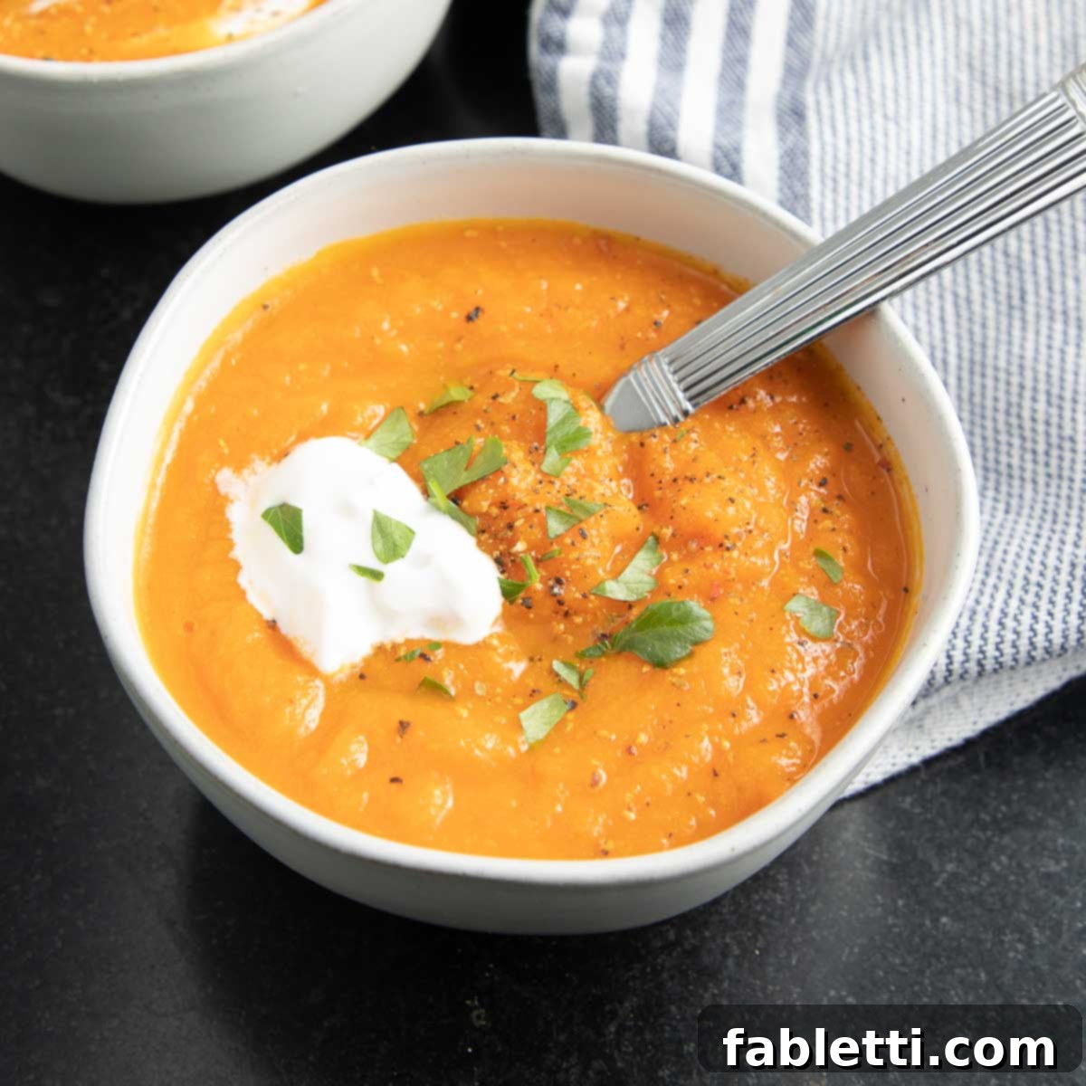 Golden Vegan Carrot Ginger Soup 3 A beautifully presented bowl of creamy carrot soup, topped with a swirl of vegan sour cream and a sprinkle of fresh vibrant herbs.