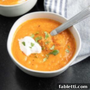 Golden Vegan Carrot Ginger Soup 18 Creamy carrot ginger soup in a bowl with a dollop of cream and fresh herbs for garnish.