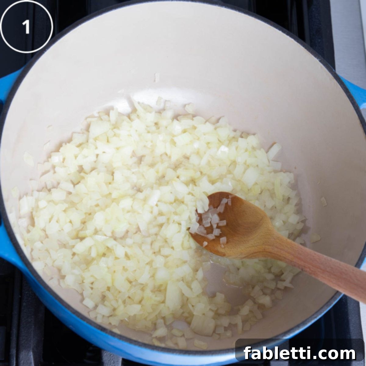 Golden Vegan Carrot Ginger Soup 8 Finely chopped onions are shown in a large Dutch oven on the stove, accompanied by a wooden spoon.