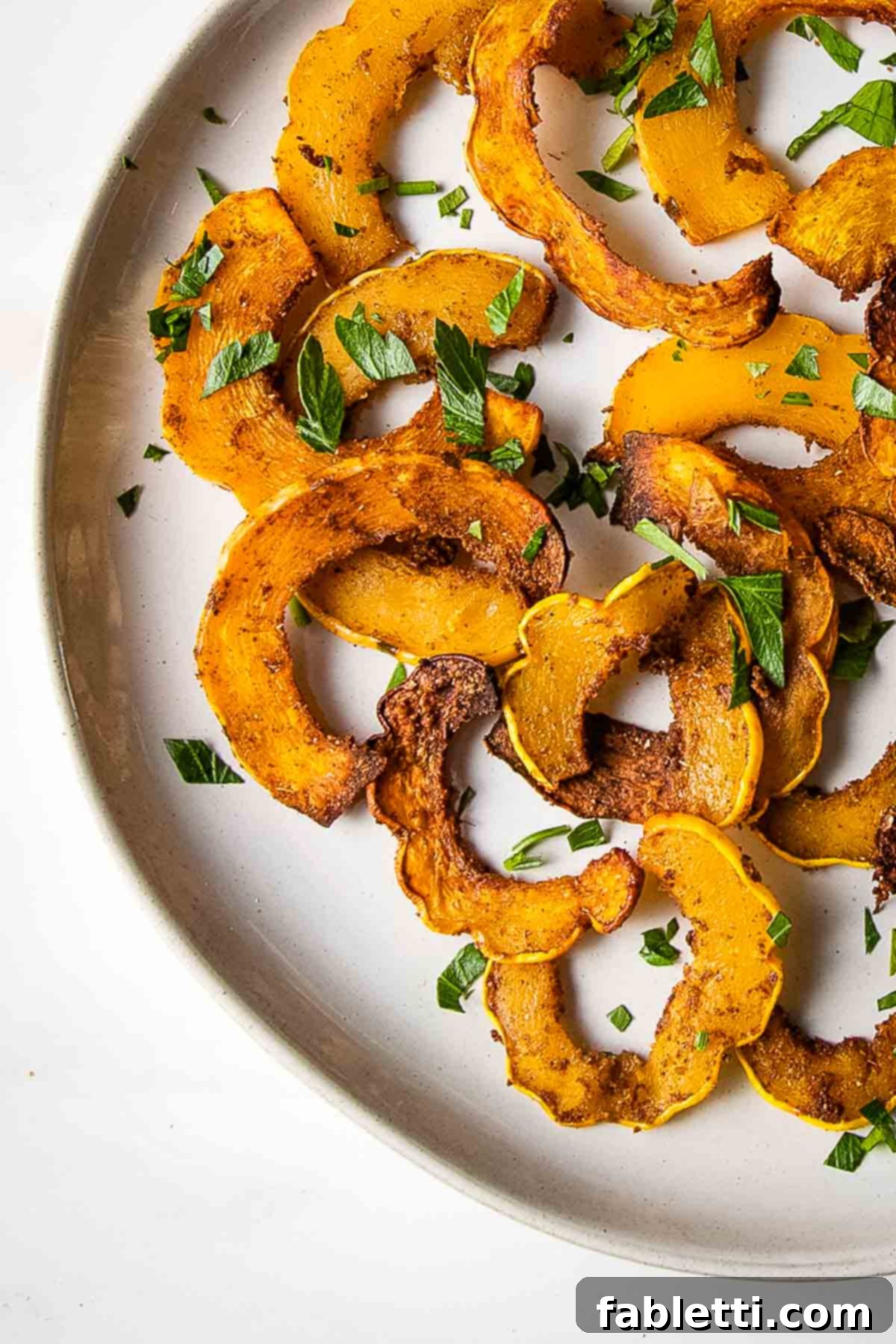 Golden Roasted Delicata Squash 2 Half moon shaped roasted delicata squash with spices on a white plate.