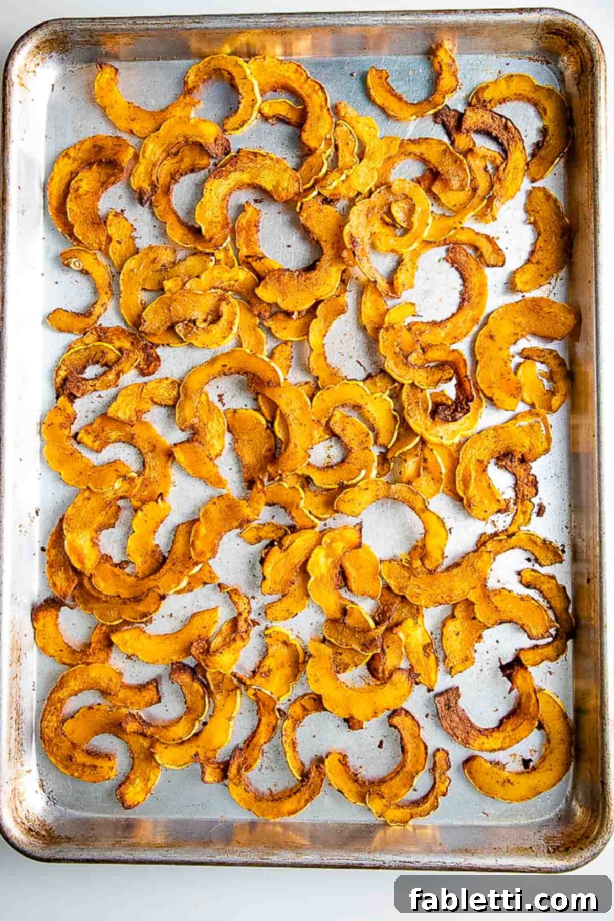 Golden Roasted Delicata Squash 10 Roasted and spiced delicata squash half moons on a baking tray.