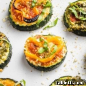 Mini Zucchini Pizzas 13 Close up of a few sliced zucchini pizza bites on a white tray. One has red sauce, a sliced yellow pepper and some fesh basil, another has pesto and roasted red pepper.