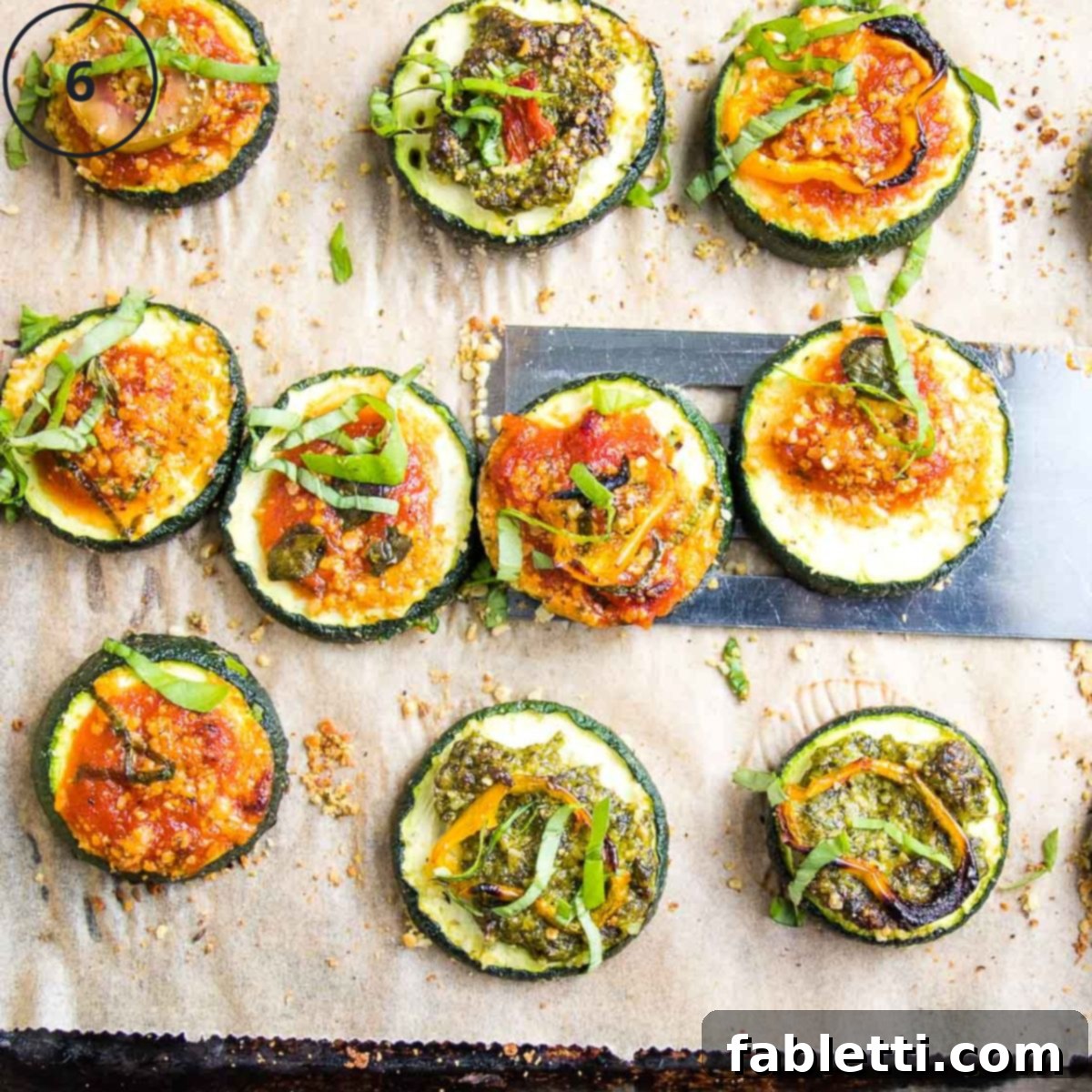 Mini Zucchini Pizzas 10 Zucchini Pizza Bites with pesto or marinara and assorted toppings, on a baking tray.