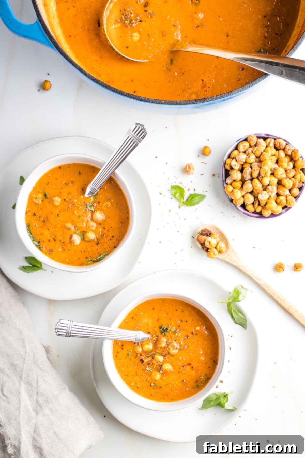 Creamy Vegan Tomato Soup 2 Bowls of creamy dairy-free tomato soup garnished with crunchy chickpeas and fresh herbs.