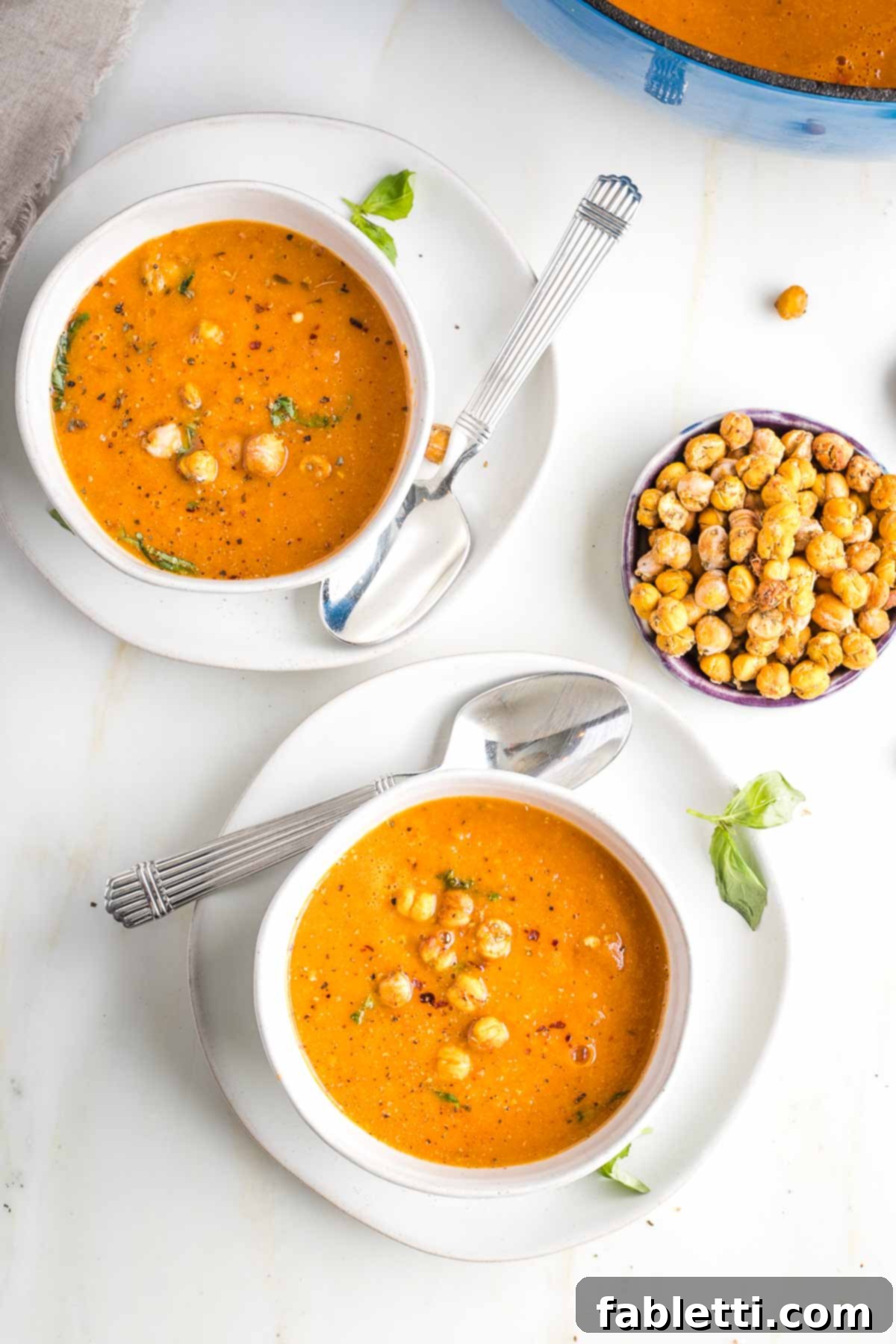 Creamy Vegan Tomato Soup 13 Two bowls of creamy tomato soup served with a separate bowl of crunchy chickpeas for garnish.