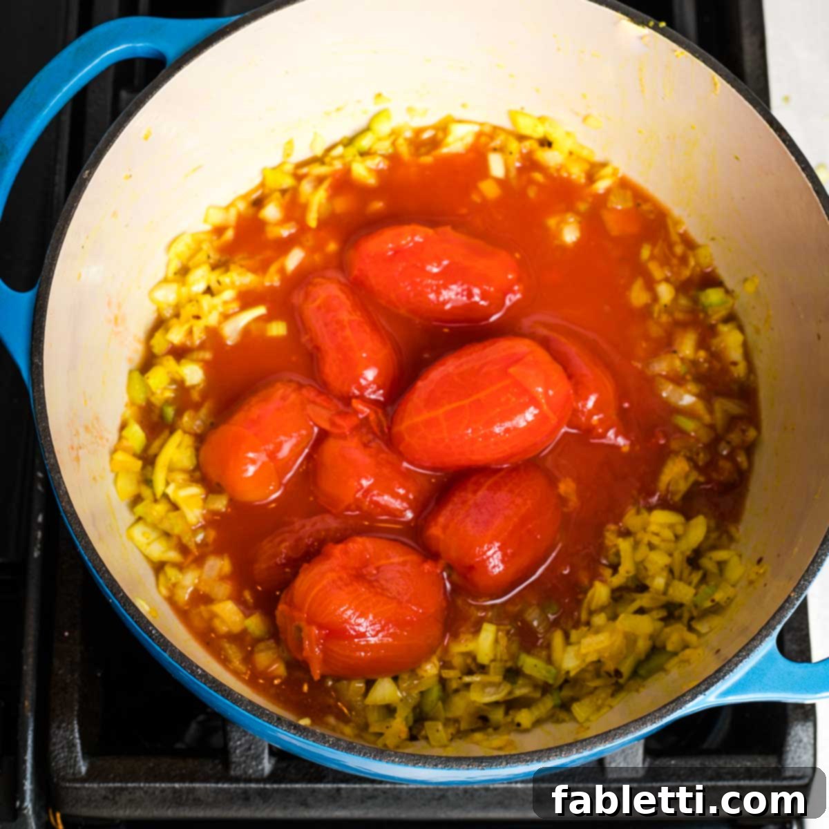 Creamy Vegan Tomato Soup 7 Dutch oven with whole tomatoes floating in broth with onions and celery.