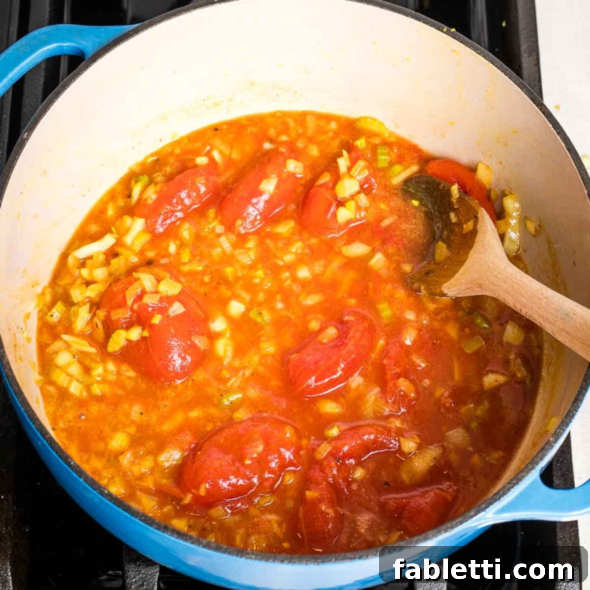 Creamy Vegan Tomato Soup 8 Squishing whole tomatoes with the back of a wooden spoon in a dutch oven for soup.