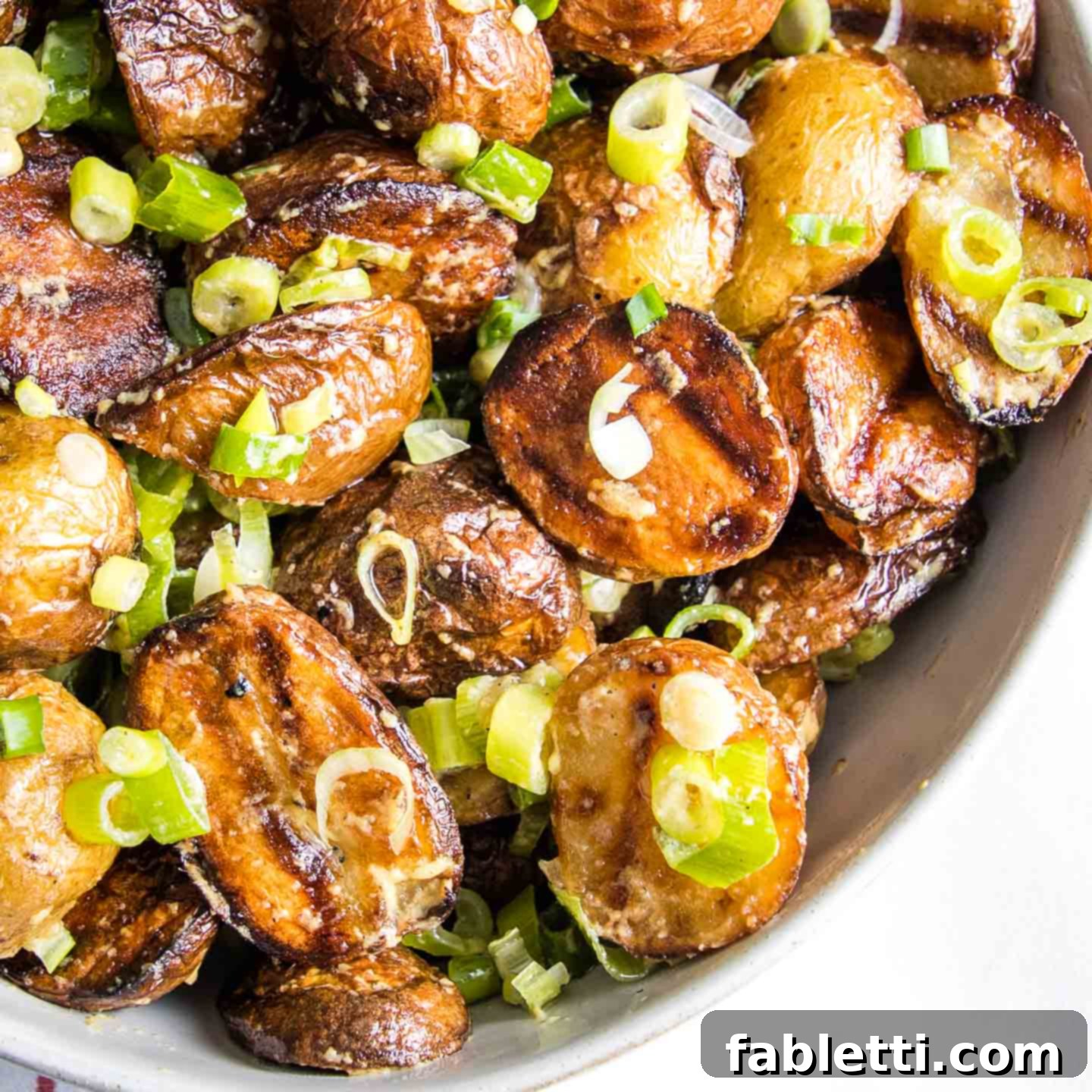 Smoky Grilled Potato Salad 2 close up quarter of a white bowl loaded with grilled potato salad with scallions.