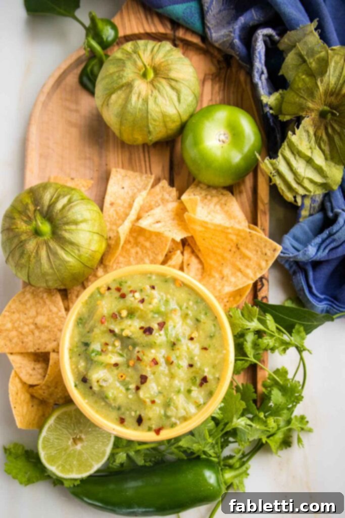 Fire-Kissed Tomatillo Salsa Verde 2 Green tomatillo salsa verde in a small bowl, surrounded by tortilla chips, fresh cilantro and tomatillos.