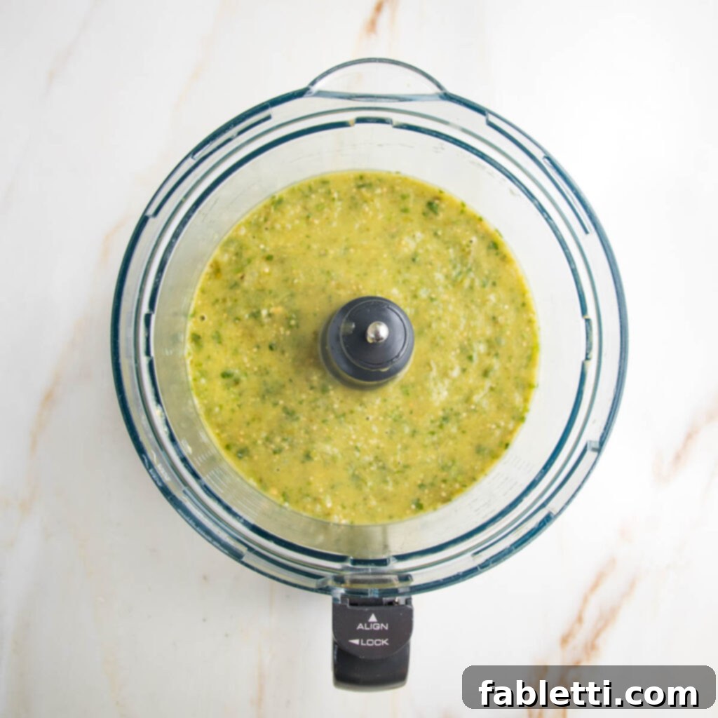 Fire-Kissed Tomatillo Salsa Verde 11 A small spoon scooping freshly blended salsa verde from a food processor bowl.