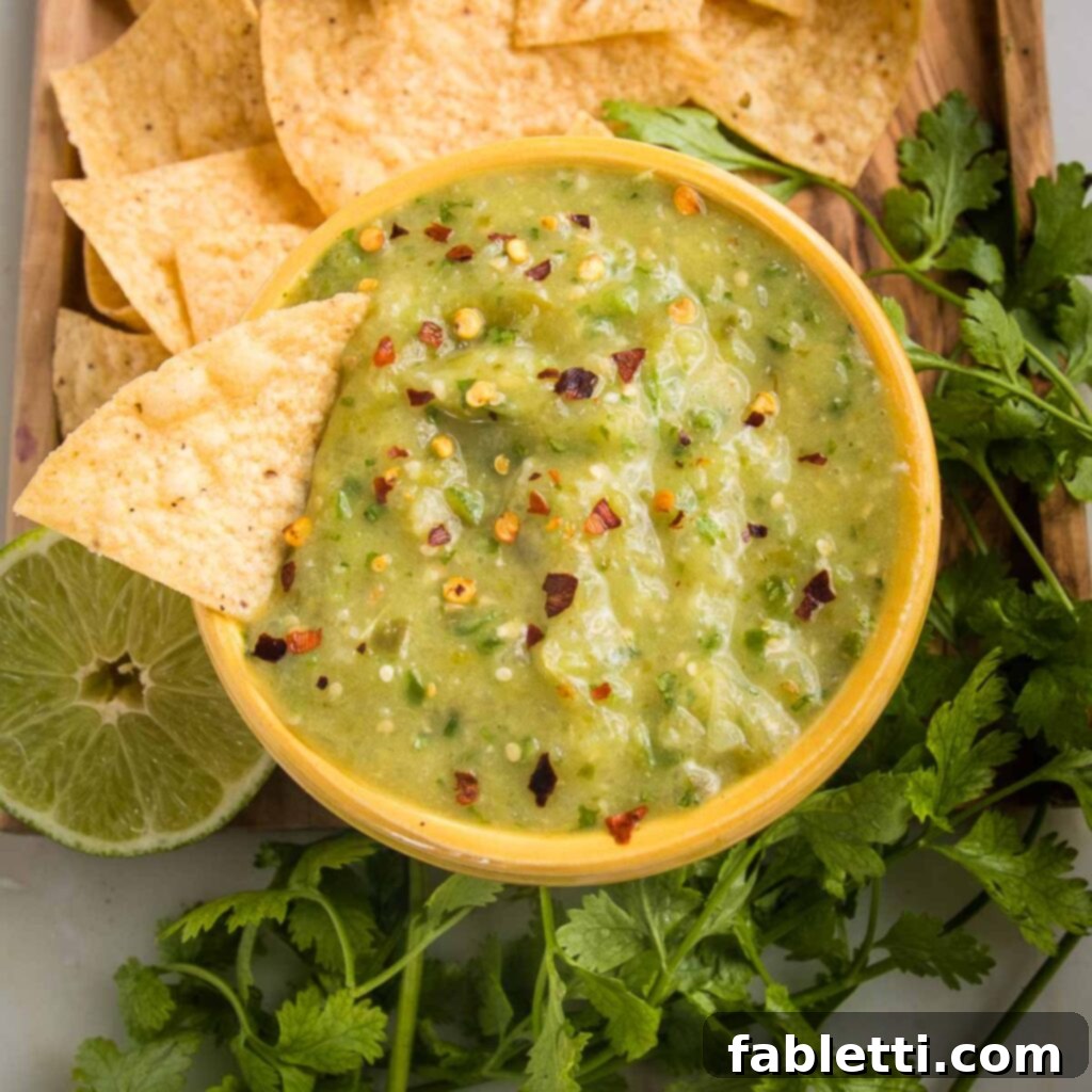 Fire-Kissed Tomatillo Salsa Verde 12 Small bowl of tomatillo salsa sprinkled with crushed red pepper. Fresh cilantro, half a lime and tortilla chips surround the salsa bowl.