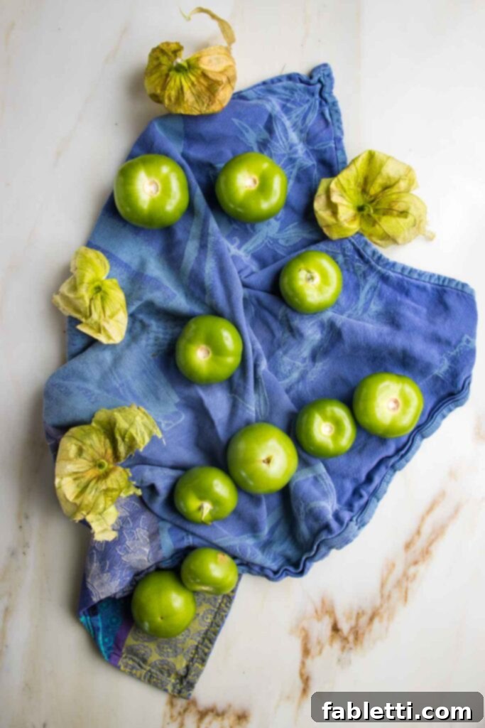 Fire-Kissed Tomatillo Salsa Verde 4 Fresh tomatillos with their papery husks removed, resting on a blue patterned dish towel.