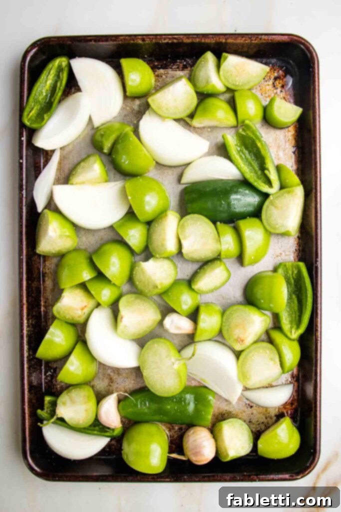Fire-Kissed Tomatillo Salsa Verde 6 Close-up of fresh tomatillos and a sliced white onion on a baking sheet, ready for roasting.