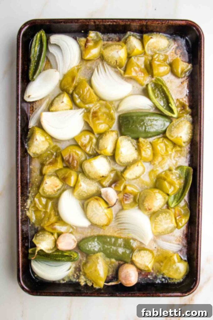 Fire-Kissed Tomatillo Salsa Verde 7 Roasted tomatillos, onions, and jalapeños with garlic cloves on a baking sheet, showing light charring.