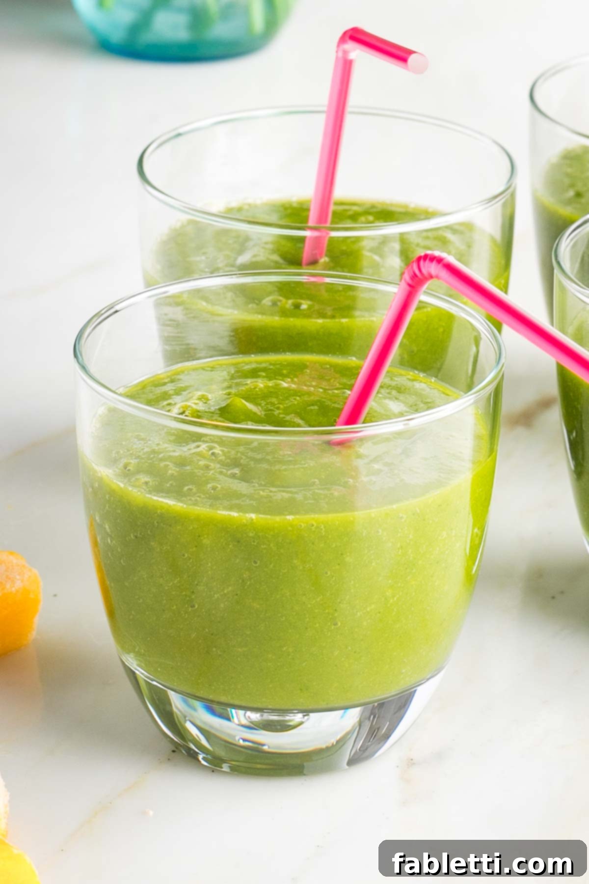 Green smoothie in short glasses with pink straws.