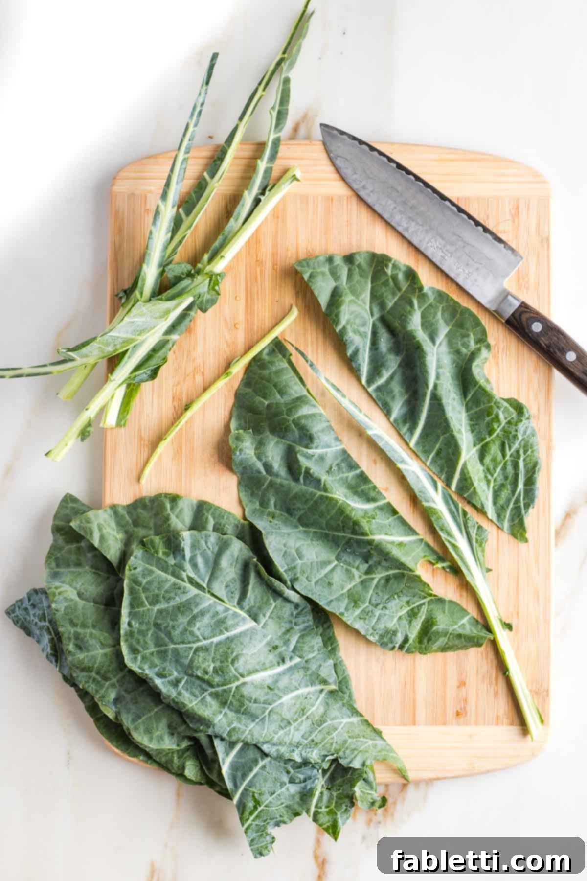 Chef's knife cutting the woody middle stem out of a large collard green leaf.