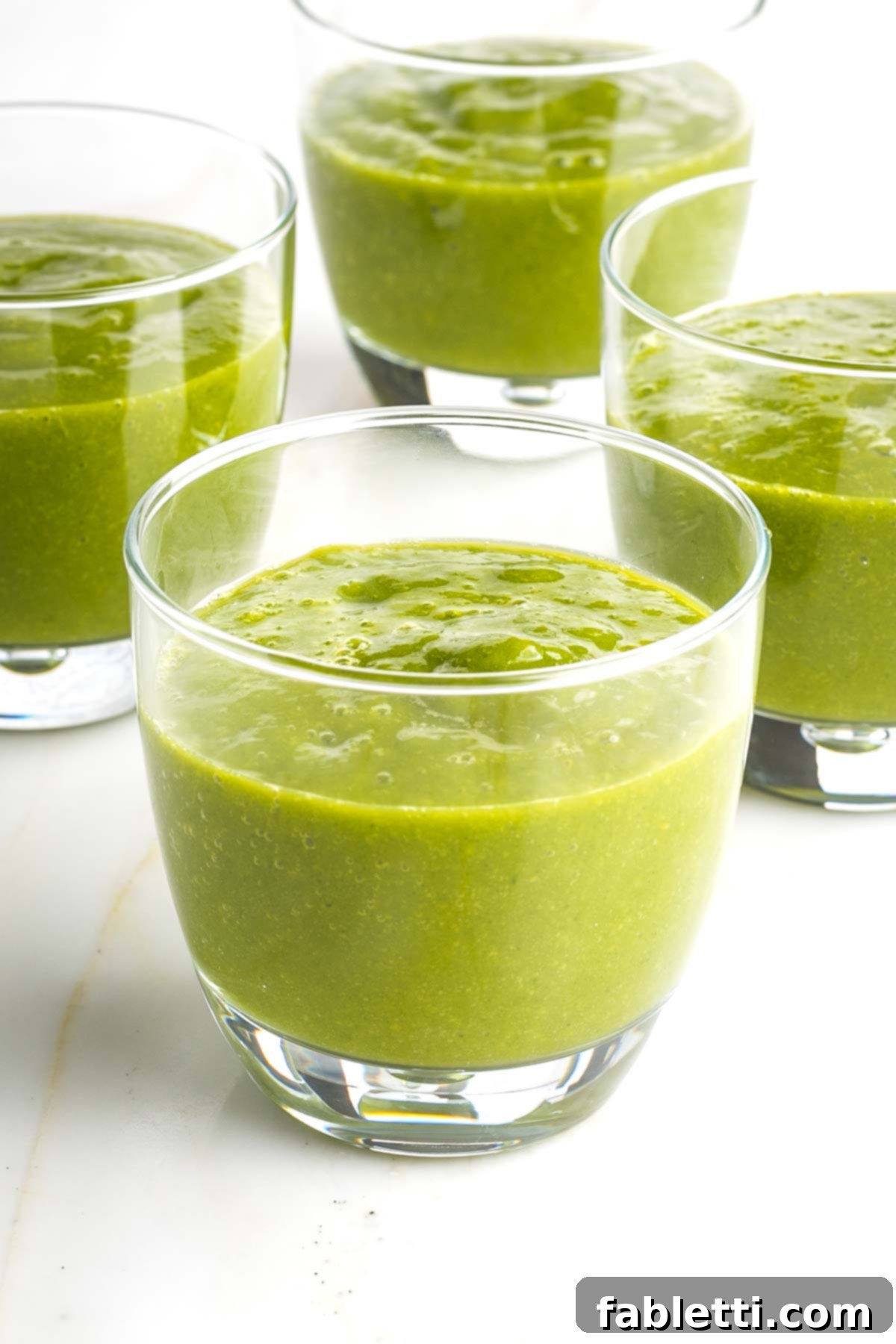 Two glasses of fresh green mango smoothie with pink straws, ready to drink.