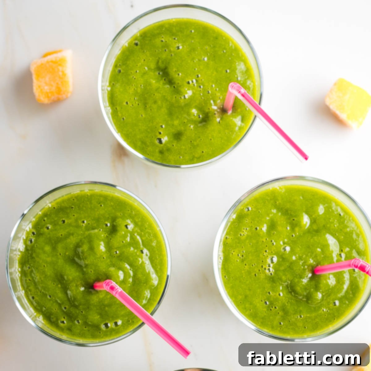 Three glasses of green smoothies, with pink straws.