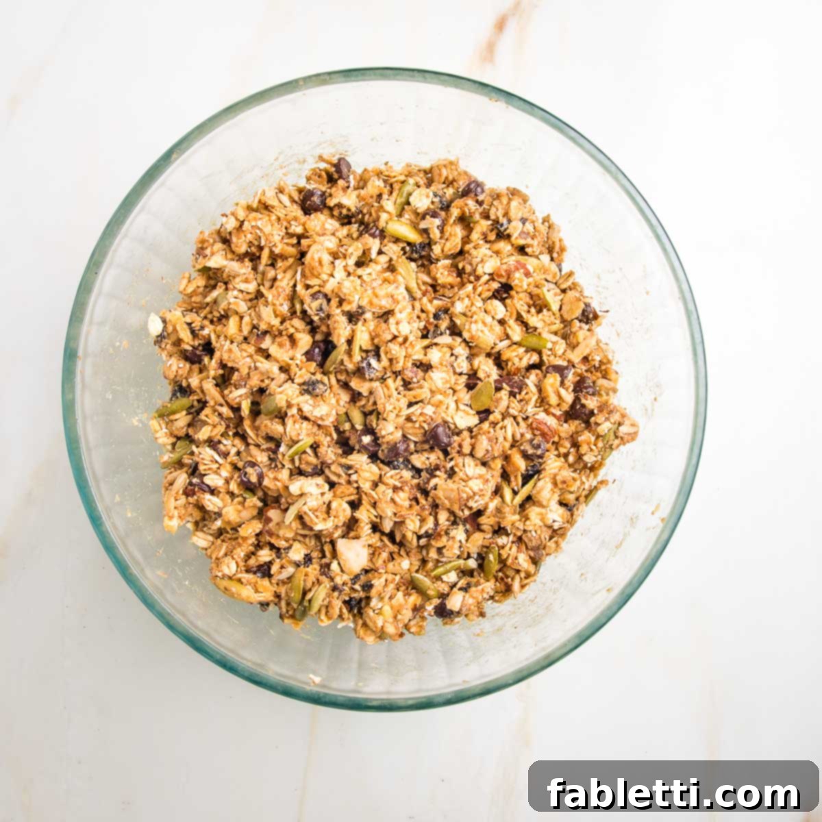 Golden Baked Granola Bites 12 Thick and pasty granola bar batter with oats, nuts, seeds, chocolate chips, and raisins, thoroughly mixed.