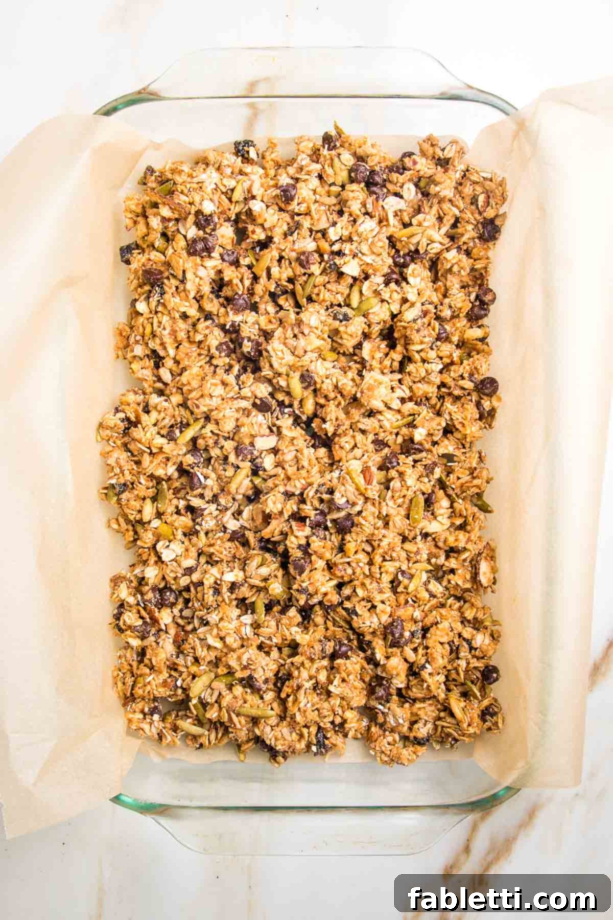 Golden Baked Granola Bites 13 Granola bar mixture spread evenly into a glass baking dish lined with parchment paper.