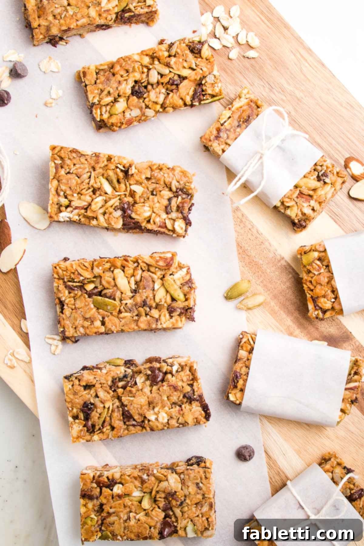 Golden Baked Granola Bites 18 Crunchy granola bars lined up on a sheet of parchment on top of a wooden board. There are a few wrapped in parchment strips with a kitchen twine tied around it.