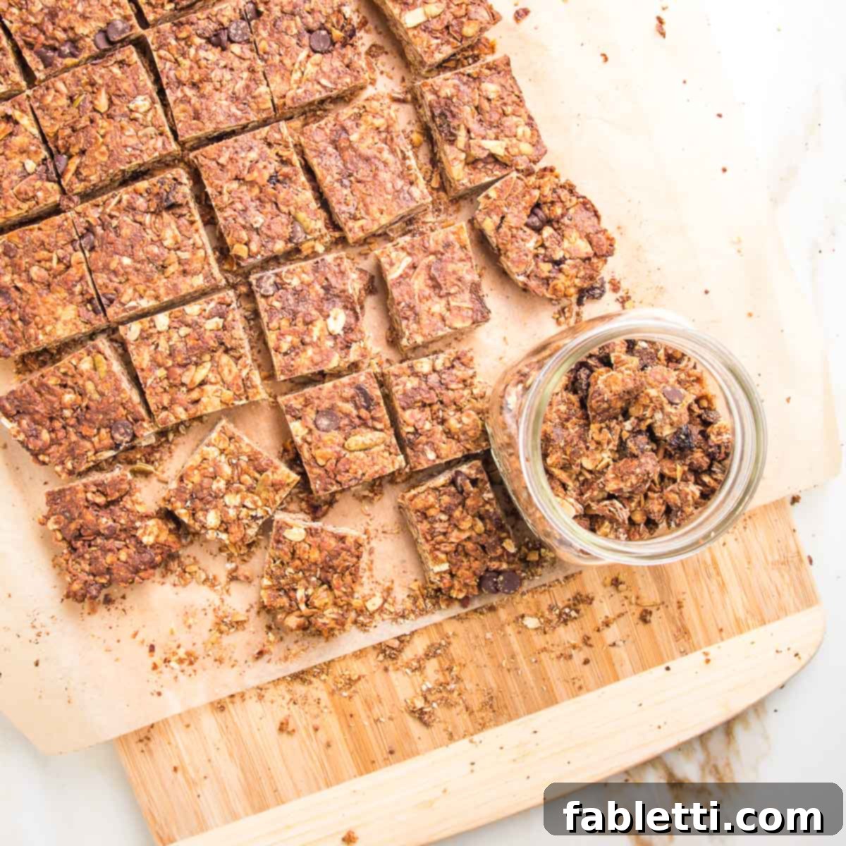 Golden Baked Granola Bites 19 Granola bars cut into squares, with lots of crumbs and a glass container holding the granola crumbs.