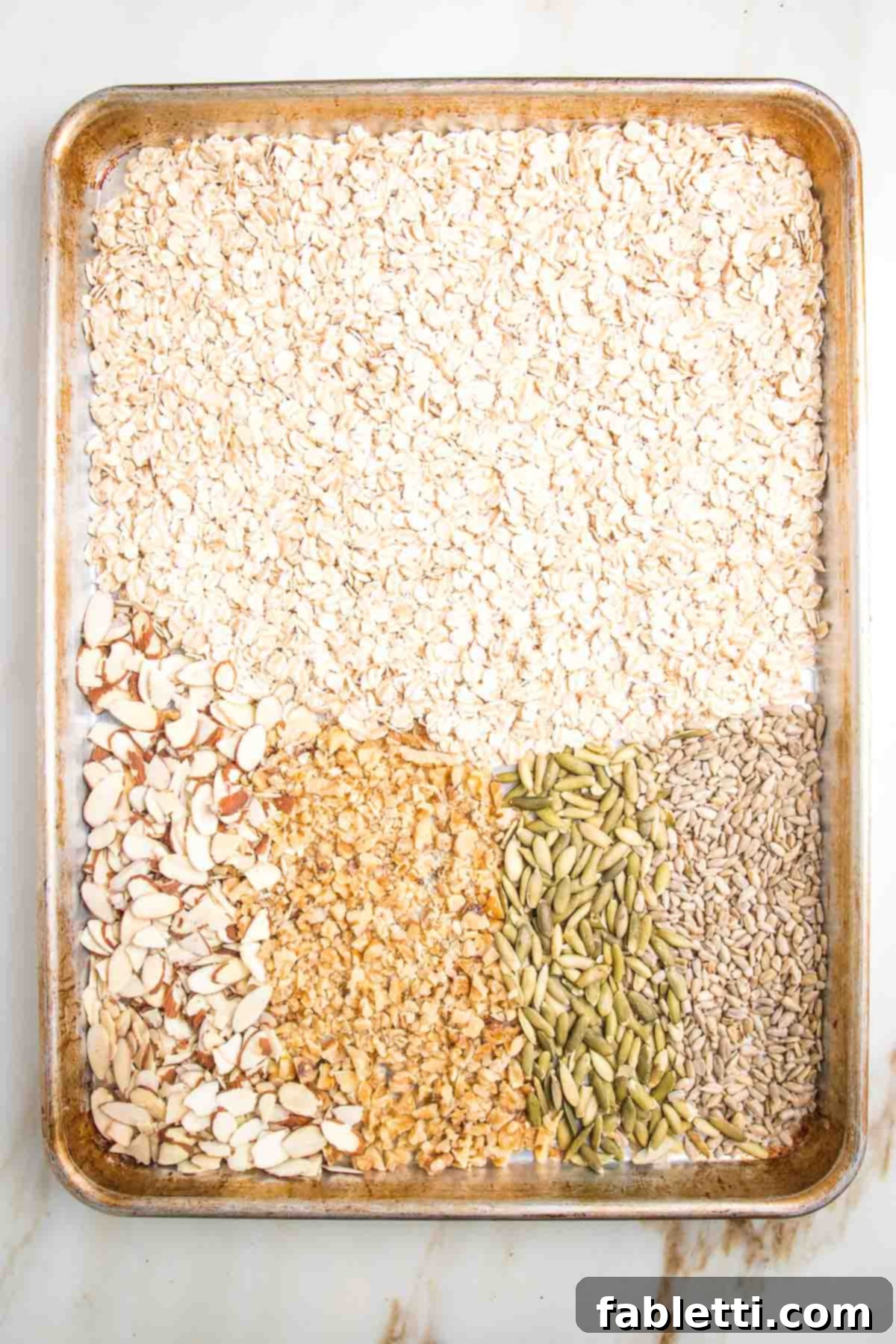 Golden Baked Granola Bites 5 Oats, nuts, and seeds spread in a single layer on a large rimmed baking tray, ready for toasting.