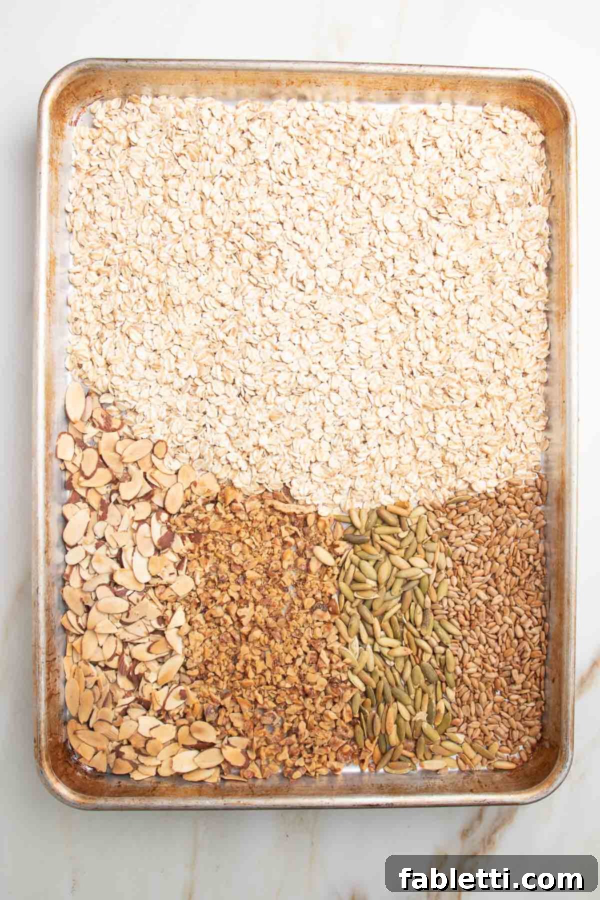 Golden Baked Granola Bites 6 Large rimmed baking tray with toasted oats, sliced almonds, chopped walnuts, sesame seeds and pumpkin seeds, golden brown after baking.