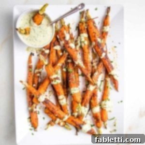 White platter with whole roasted and coated with spices carrots. A small glass bowl of dipping sauce with a few carrots in there and a spoon. The sauce is greenish and it's also drizzled on the cooked carrots. There are fresh herbs scattered around.