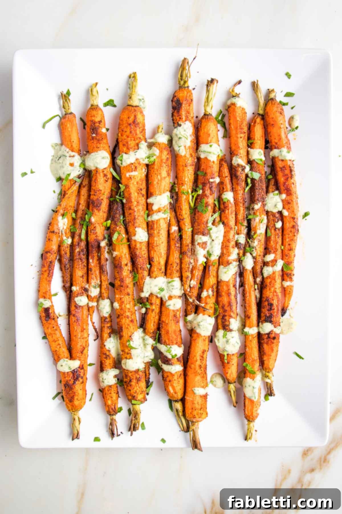 White platter with whole roasted carrots, drizzled with green tahini sauce. 